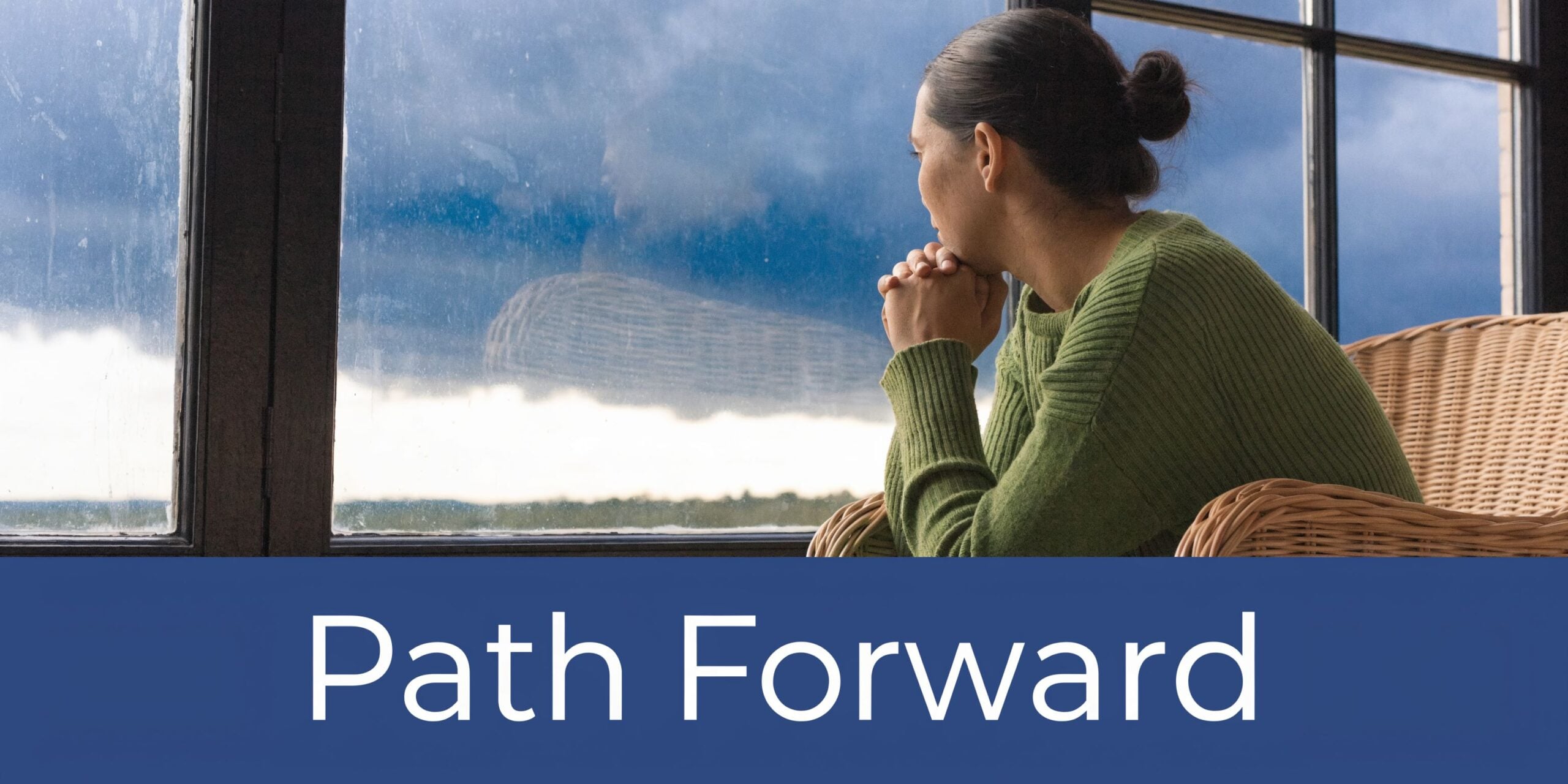 A thoughtful woman in a green sweater sits by a window, reflecting on her path forward.