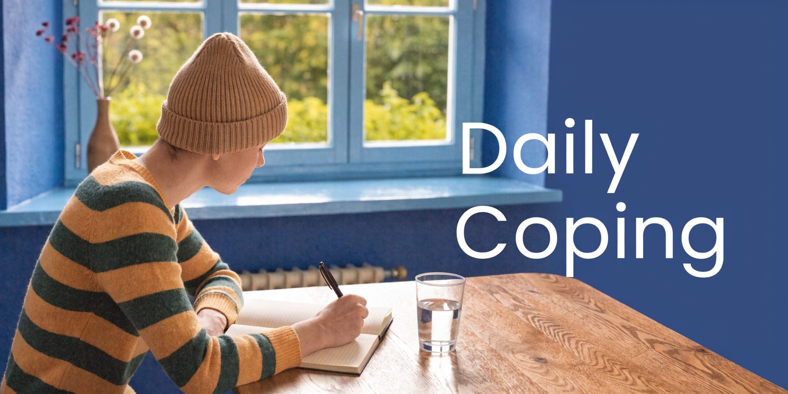 A person wearing a beanie writing in a journal at a wooden table next to a water glass.