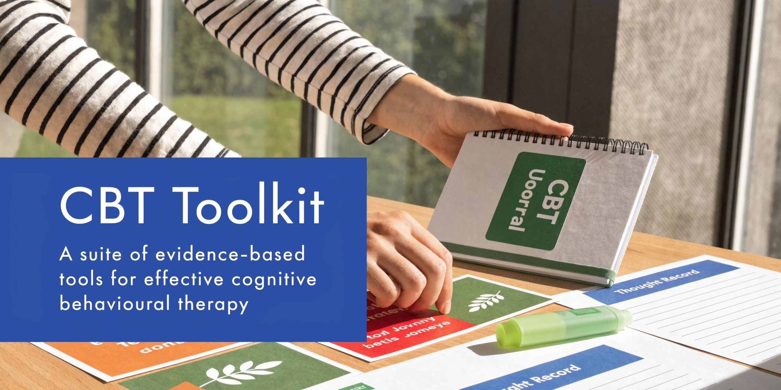 A person using cognitive behavioral therapy tools and a thought record sheet on a wooden desk.