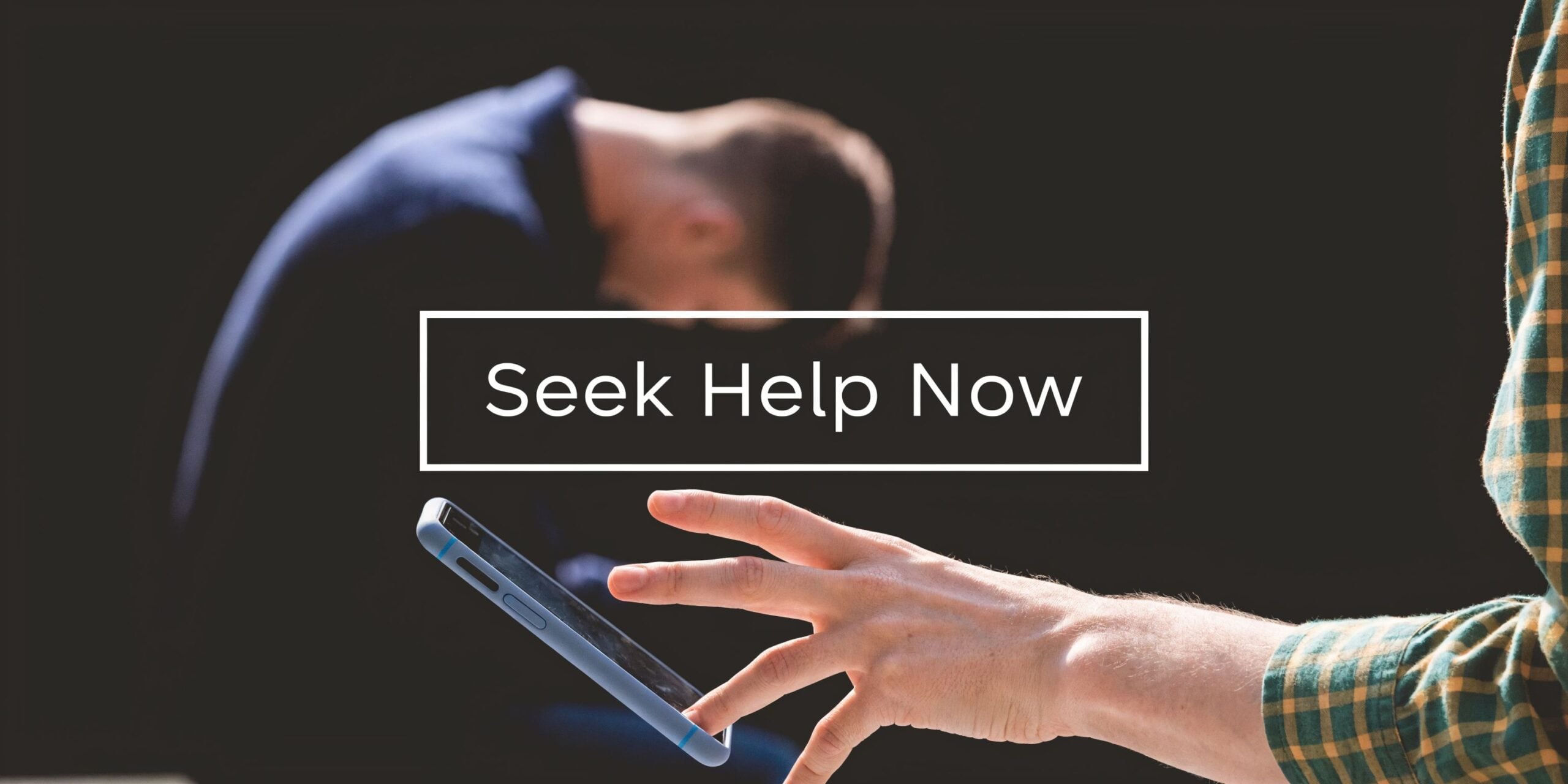 A distressed man sits in the background while someone reaches for a smartphone to find support resources.