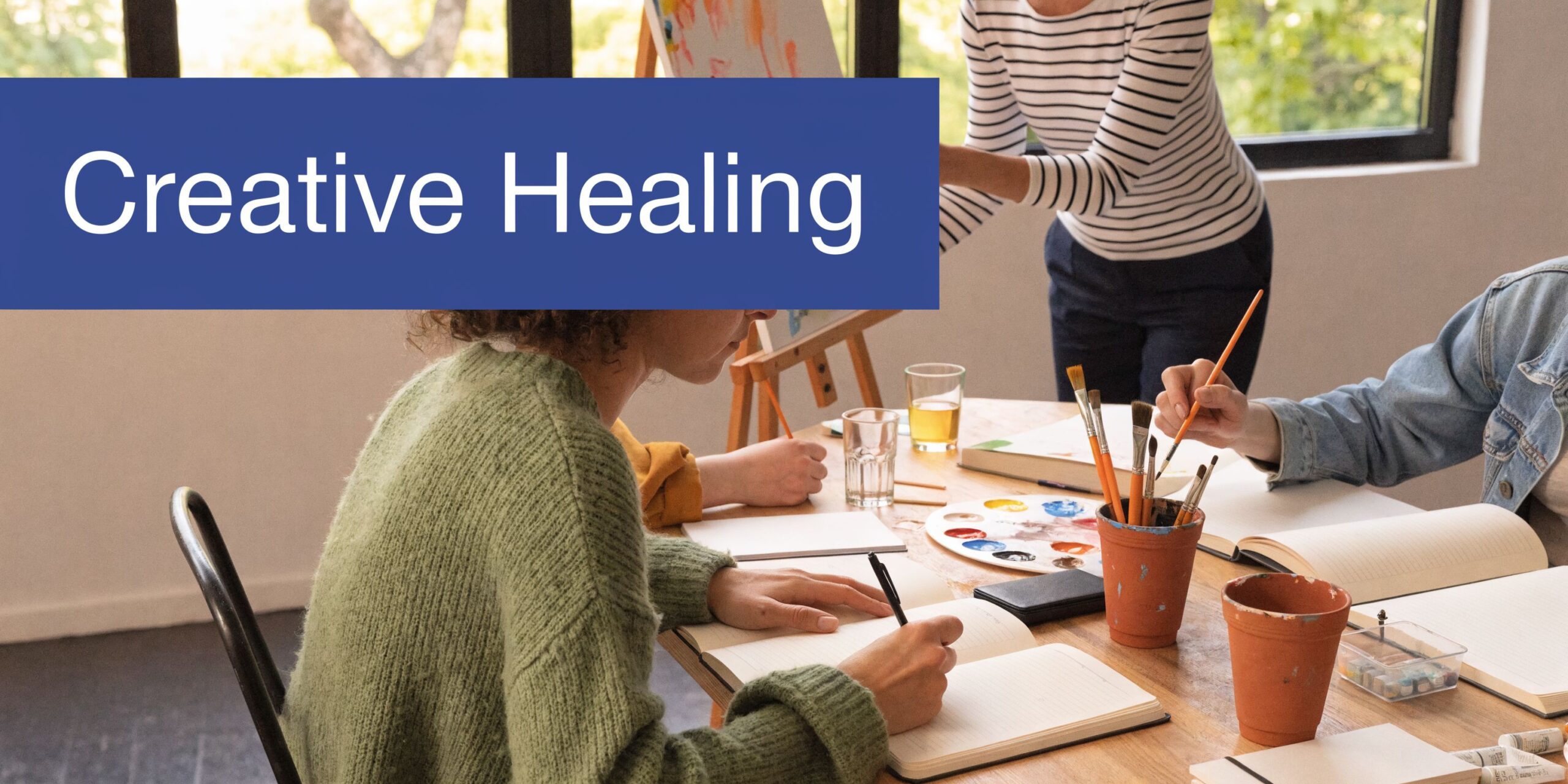 A person writing in a notebook during a creative group healing therapy session with art supplies.