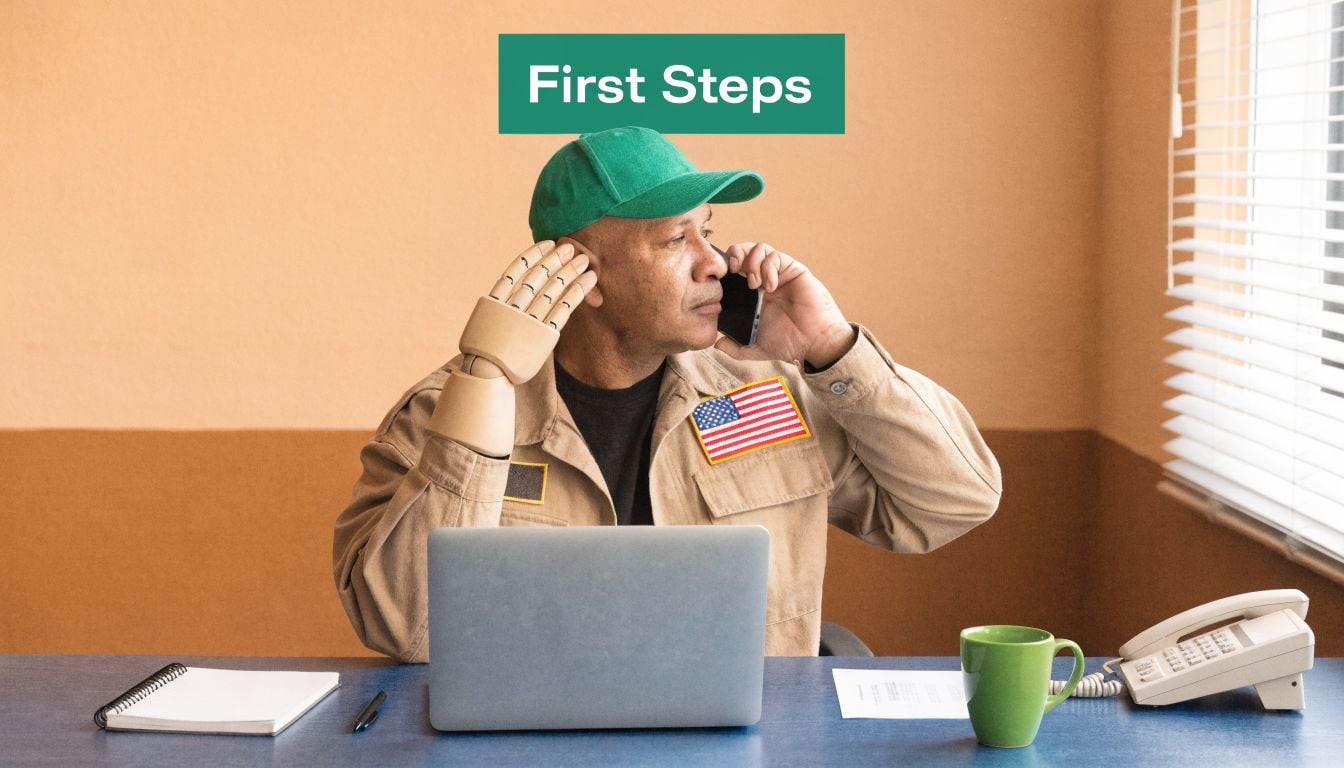 A veteran with a prosthetic arm wearing a green cap makes a phone call at a desk.