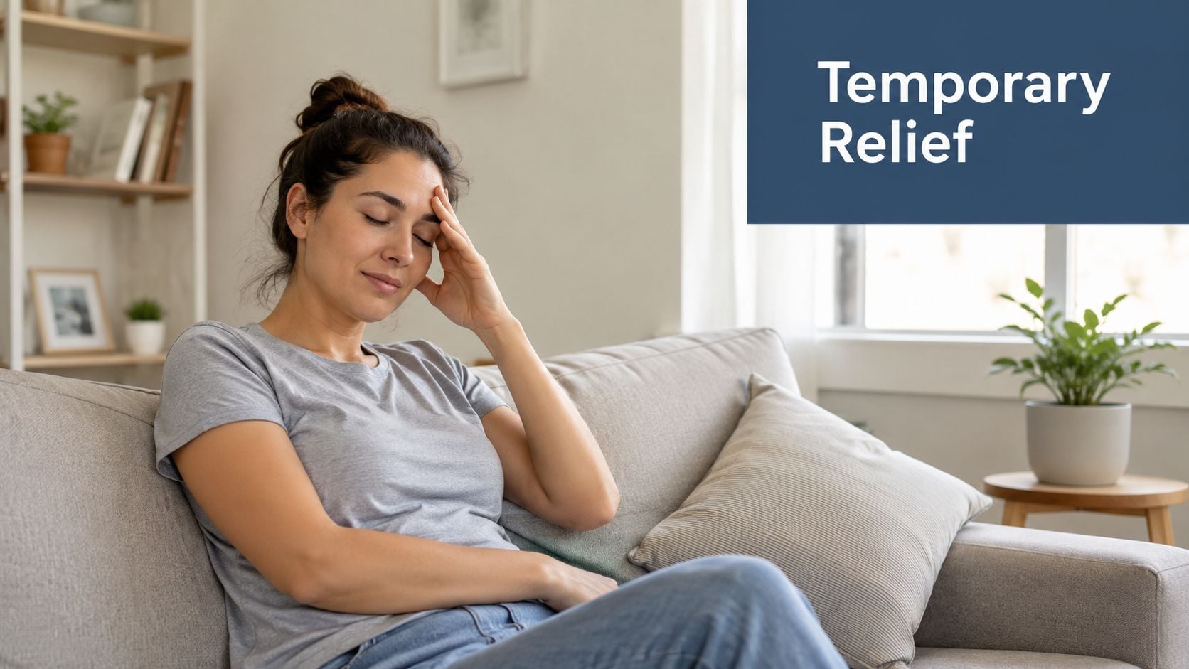 A woman sitting on a gray couch looking stressed with her hand on her forehead