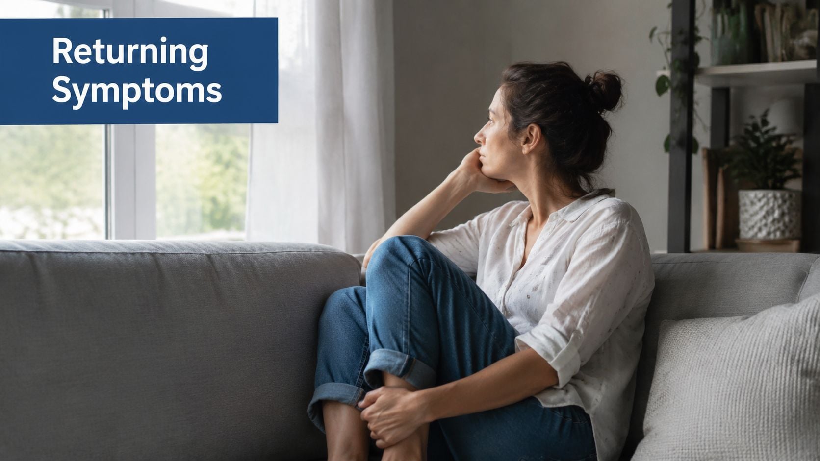 A pensive woman sitting on a couch looking out a window, reflecting on returning health symptoms.